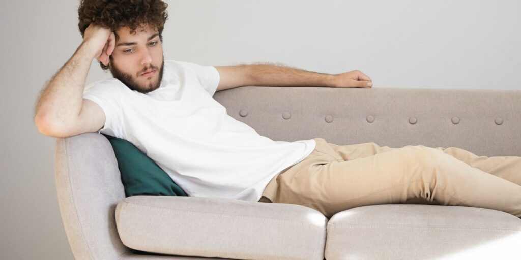 homem sentado na cama ou no sofá, com expressão de desconforto e preocupação