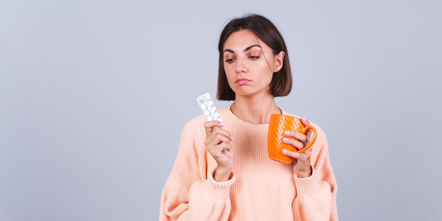 mulher com expressão de dúvida segurando uma cartela de medicamento